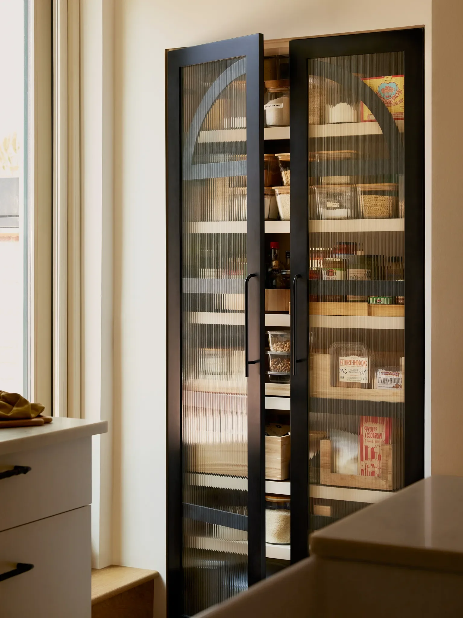 The built-in pantry was a new addition to the space. Reeded glass creates a visual lightness to the cabinetry; the curved elements echo the rounded glass panes of the front door.