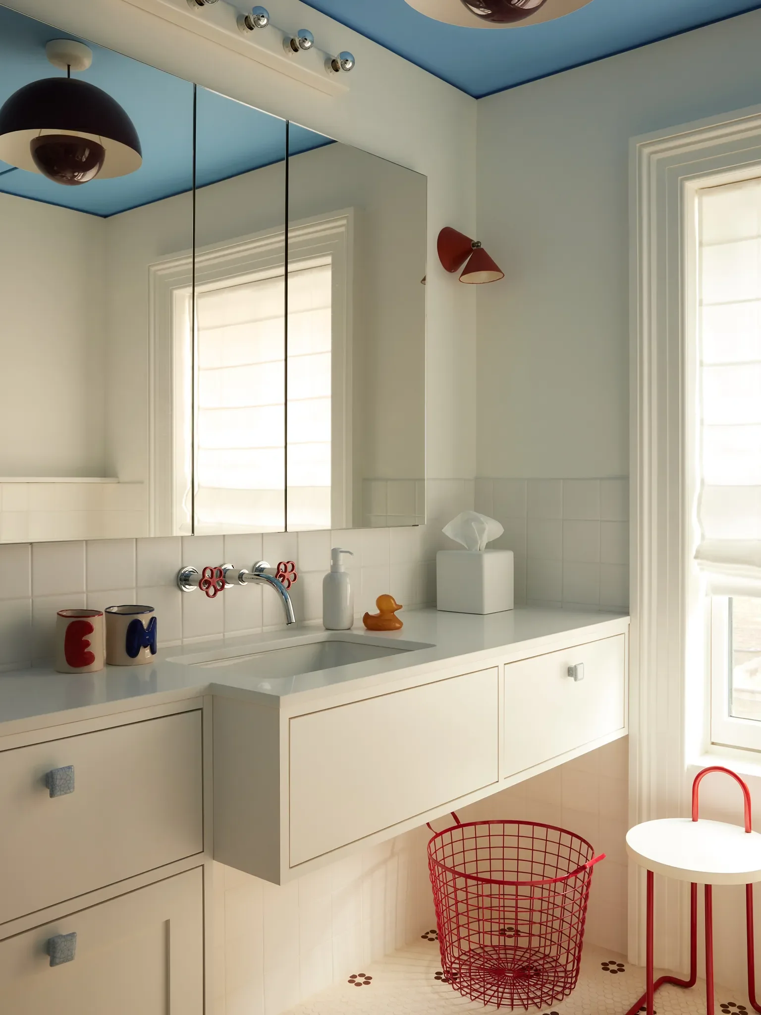 Custom cabinetry maximizes the footprint of this third-story full bathroom, which is shared by the clients’ children. “The mix of the chrome and the bright red has a sort of utilitarian feel to it,” s